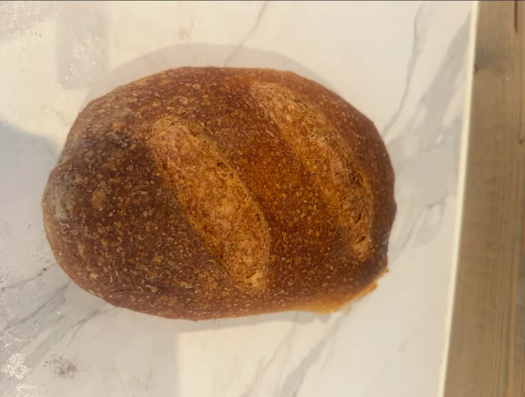 Et rundt fullkornsbrød med brun skorpe på bakepapir.